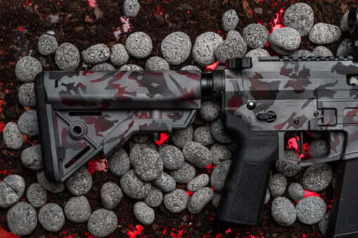 Detail of UDP-9 Rifle in Scorched Earth Cerakote B5 Systems Bravo Stock laying on lava rocks